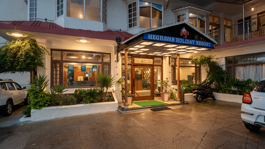 A photo of the entrance to DLS Meghavan Resort, showing the building's facade, entrance way, and some potted plants.